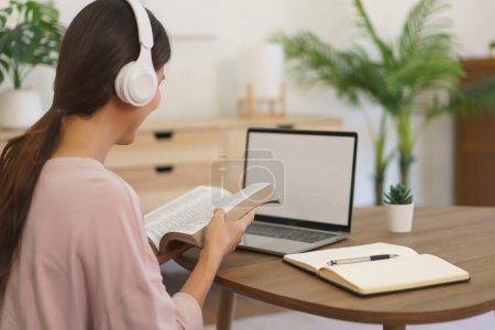 Téléchargez les photos : Femme entrepreneur dans le casque pour écouter de la musique et de travailler à la maison avec la lecture de livre d'affaires. - en image libre de droit