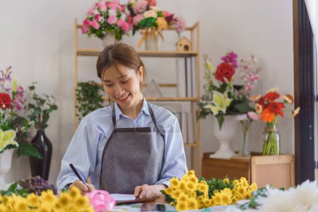 Téléchargez les photos : Concept de fleurisme, Fleuriste femme écrivant des commandes et des informations client dans le carnet à la boutique de fleurs. - en image libre de droit