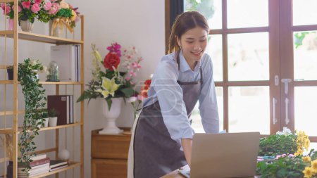Téléchargez les photos : Florist concept, Woman florist checking customer order on laptop while working in flower shop. - en image libre de droit
