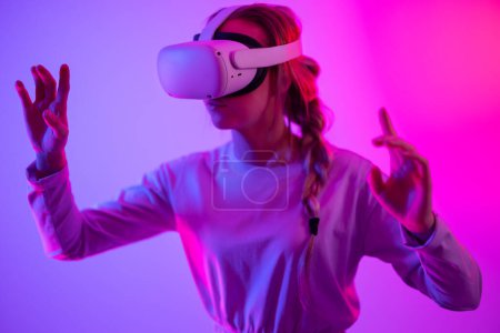 Photo for Exploring around the metaverse using VR. Young woman exploring immersive technology in a studio playing 3D game while wearing a virtual reality headset. - Royalty Free Image