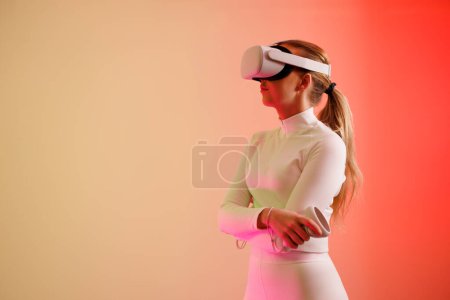 Photo for Young woman wearing VR glasses standing with arms crossed against colored background - Royalty Free Image