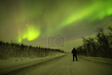 Silhouette eines einsamen Beobachters unter den faszinierenden Nordlichtern und Sternen in der Arktis.