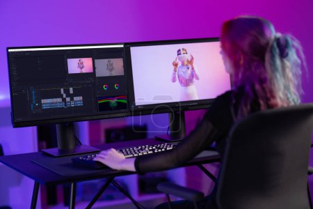 Professionelle kreative digitale Künstler in der Videobearbeitung eingetaucht, umgeben von lebendigen Neonlichtern in modernen Büroräumen.
