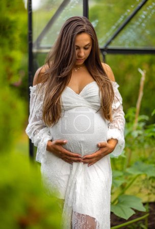 A peaceful image of a pregnant woman, dressed in a white lace gown, gently holding her belly in a lush garden setting, evoking a sense of anticipation and maternal love.