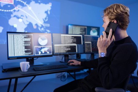 Cybersicherheitsanalyst in einem Operationszentrum für Cyber-Sicherheit SOC in einem wichtigen Telefonat. Mehrere Bildschirme mit Karte, Unfallprotokollen und Alarmdaten.
