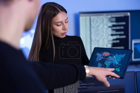 Close-up of a cyber security team working in a Cyber Security Operations Center SOC. Woman work as Chief Information Security Officer CISO and manager pointing on a real time map om tablet.