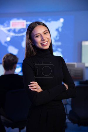 Smiling confident female Cyber Security Analyst or Manager in enterprise Security Operations Center SOC. A team of security operators working with cybersecurity incidents and alerts.