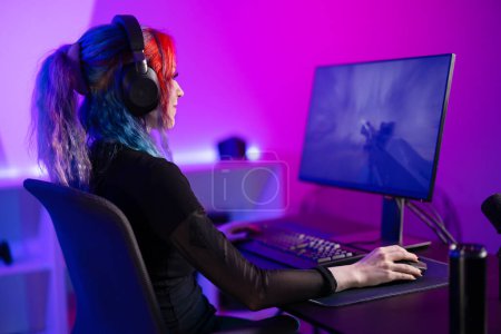 Jugador profesional que juega intensamente un videojuego de disparos en primera persona FPS, rodeado de una vívida iluminación púrpura en una moderna configuración de sala de juegos.