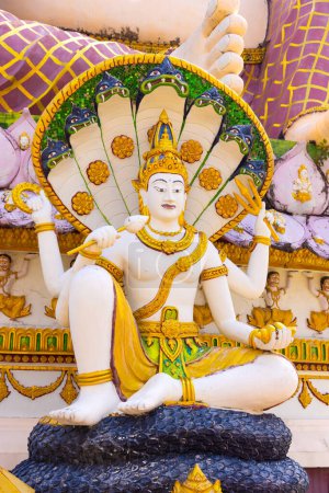 Eine lebendige und detaillierte Statue einer thailändischen Gottheit mit mehreren Armen, geschmückt mit traditioneller Kleidung, vor Tempelhintergrund in Thailand.