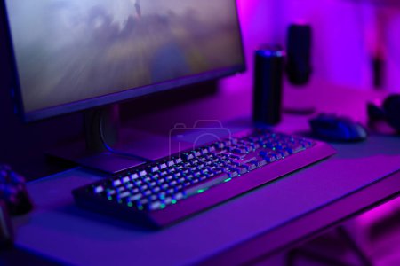 Primer plano de una estación de trabajo de juegos con un teclado elegante, ratón y monitor bajo una vibrante iluminación led púrpura. Configuración ideal para jugadores o entusiastas de la tecnología.