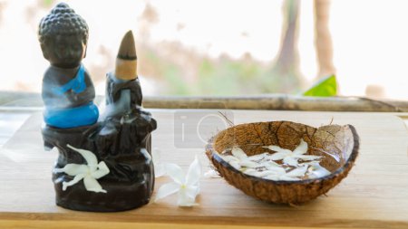 Téléchargez les photos : Encens fumant sur une figurine de Bouddha avec décoration florale, traditions orientales. Photo de haute qualité - en image libre de droit