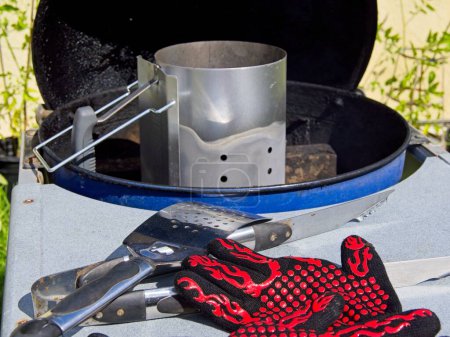 Photo for Preparations for grilling; tools, gloves, charcoal chimney on the backyard grill - Royalty Free Image