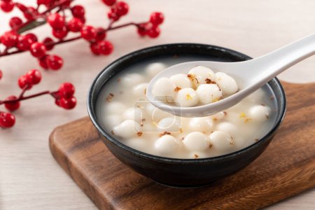 Little white tangyuan (tang yuan, glutinous rice dumpling balls) with sweet osmanthus honey and syrup soup in a bowl on wooden table background.