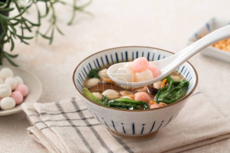 Foto de Comer tangyuan pequeño rojo y blanco, tang yuan, bolas de masa de arroz glutinoso con sopa salada en un tazón sobre fondo de mesa blanco. - Imagen libre de derechos