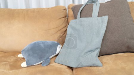 Une peluche de pingouin gris et un sac fourre-tout gris sur un canapé.