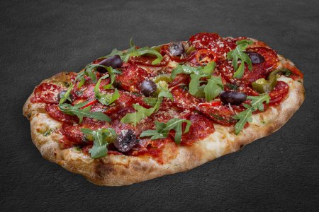 Pizza Diavolo mit Chorizo, Rucola, Jalapeño, Chili, Kalamata, Pesto. Römische Pizza rechteckig auf dunklem Hintergrund
