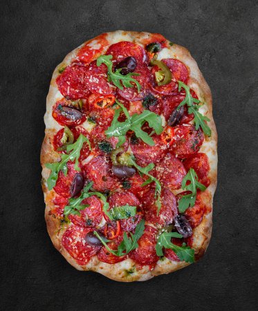 Pizza Diavolo with chorizo, rucola, jalapeno, chili, kalamata, pesto. Roman pizza rectangular on dark background
