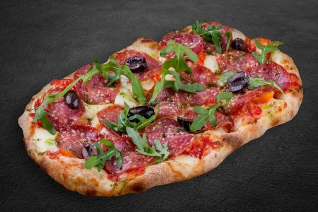 Pizza Diavolo mit Chorizo, Rucola, Jalapeño, Chili, Kalamata, Pesto. Römische Pizza rechteckig auf dunklem Hintergrund