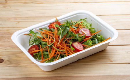 Foto de Mezcla de ensaladas (verduras, zanahorias y tomates cherry). Comida saludable. Comida para llevar. Sobre un fondo de madera. - Imagen libre de derechos