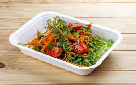Foto de Mezcla de ensaladas (verduras, zanahorias y tomates cherry). Comida saludable. Comida para llevar. Sobre un fondo de madera. - Imagen libre de derechos