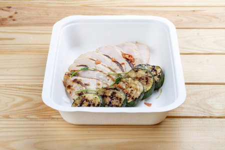 Foto de Pechuga de pollo a la plancha con calabacín. Dieta saludable. Comida para llevar. Sobre un fondo de madera. - Imagen libre de derechos