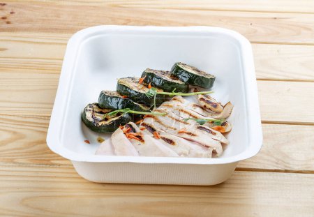Grilled chicken breast with zucchini. Healthy diet. Takeaway food.  On a wooden background.