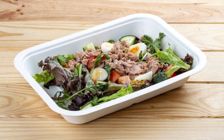 Tuna salad with tuna and quail eggs. Healthy food. Takeaway food.  On a wooden background.