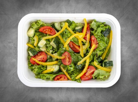 Salat mit Gurken, Tomaten und Paprika. Gesunde Ernährung. Essen zum Mitnehmen. Draufsicht, auf grauem Hintergrund.