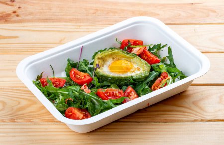 Baked egg in avocado with lettuce and tomatoes. Healthy diet. Takeaway food.  On a wooden background.