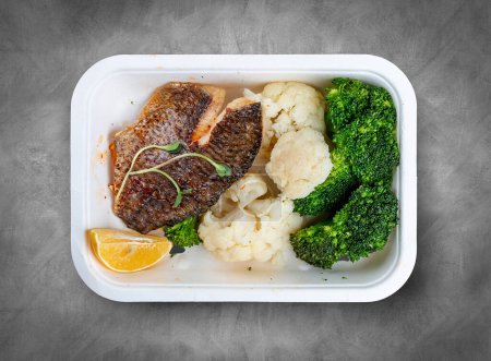 Filete de lubina, brócoli blanqueado y coliflor. Comida saludable. Comida para llevar. Vista superior, sobre un fondo gris.