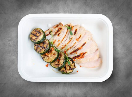 Gegrillte Hühnerbrust mit Zucchini. Gesunde Ernährung. Essen zum Mitnehmen. Draufsicht, auf grauem Hintergrund.
