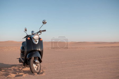 Téléchargez les photos : Le scooter noir rétro au coucher du soleil dans le sable doré du désert de Namib - en image libre de droit