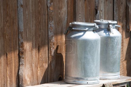 Photo for Cans of milk stand against the background of a wooden barn wall. - Royalty Free Image