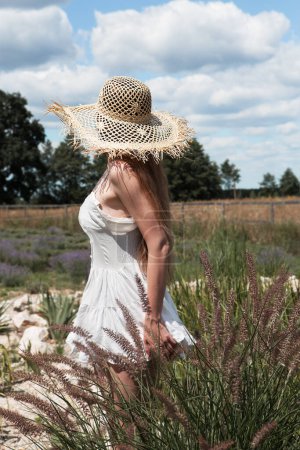 Foto de Joven sexy hermosa mujer en un sombrero de paja se da la vuelta y mira a la distancia mientras camina en el jardín contra el fondo del cielo. - Imagen libre de derechos
