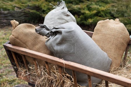 Rag bags lie on hay in a wooden cart. Retro method of transporting grain and other products.
