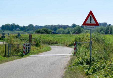 Téléchargez les photos : Panneau de signalisation hollandais "attention à une grille de bétail" devant une grille de bétail et une digue hollandaise dans un paysage européen de polders - en image libre de droit