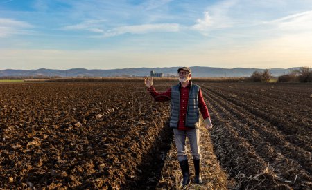 Téléchargez les photos : Senior farmer with tablet greeting someone in distance on field in late autumn time - en image libre de droit