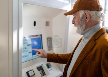 Senior man purchasing ticket from automatic machine on terminal of railway station