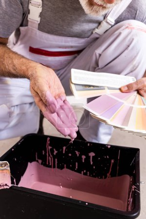Travailleur senior vérifiant la qualité de la peinture et correspondant à la palette de couleurs