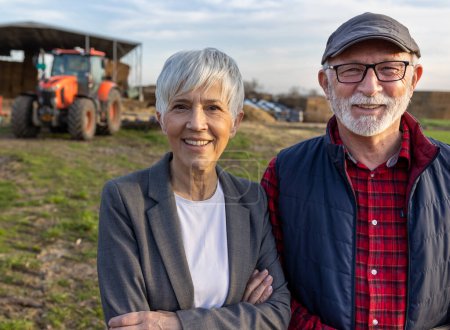 Foto de Retrato de una pareja de granjeros maduros frente al tractor en el rancho de ganado - Imagen libre de derechos