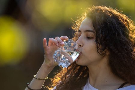 Foto de Mujer bastante joven bebiendo agua de vidrio en el parque - Imagen libre de derechos