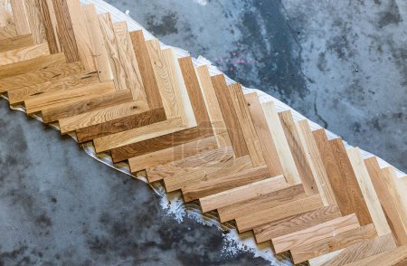 Top view of parquet boards installing in herringbone arrangement on glue, home flooring concept
