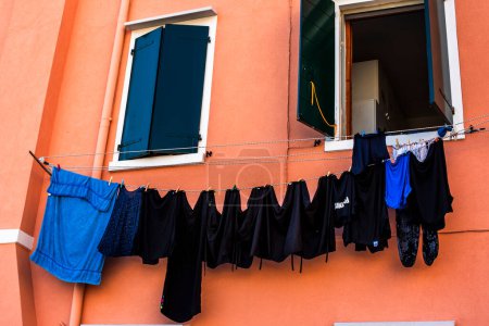 laundry hanging out in the autumn sun in the town of Pellestrina on the Venice Lagoon black t-shirts hanging on a brick-coloured wall