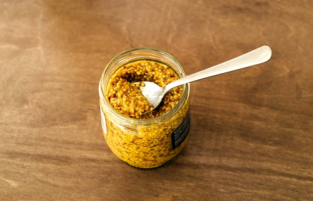 Téléchargez les photos : Open jar of french whole-grain yellow mustard with a spoon inside - top view - en image libre de droit