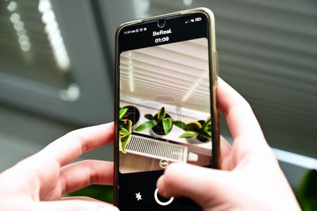 Téléchargez les photos : Lublin, Poland. 26 January 2023. Young woman's hands holding a mobile phone while taking a photo of her sansevieria plants to be posted on Be Real app - en image libre de droit