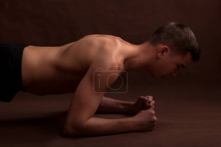 Photo for Handsome muscular shirtless adolescent doing plank exercise. - Royalty Free Image