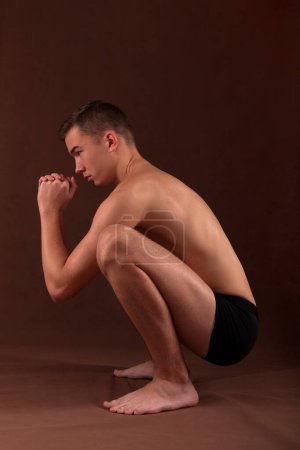 Photo for Handsome muscular shirtless adolescent shirtless boy in deep squat exercise. - Royalty Free Image