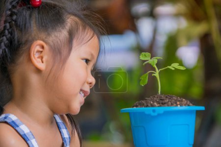 Photo for Cute children look with love at green sprout in blue pot. happy smiles and escape planted in a flowerpot. - Royalty Free Image