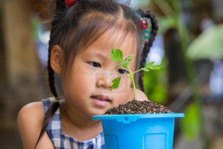 Photo for Cute children look with love at green sprout in blue pot. happy smiles and escape planted in a flowerpot. - Royalty Free Image