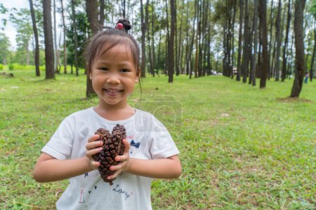 Photo for Asiand Child in the forest holds a handful of pine cones show to camera. - Royalty Free Image